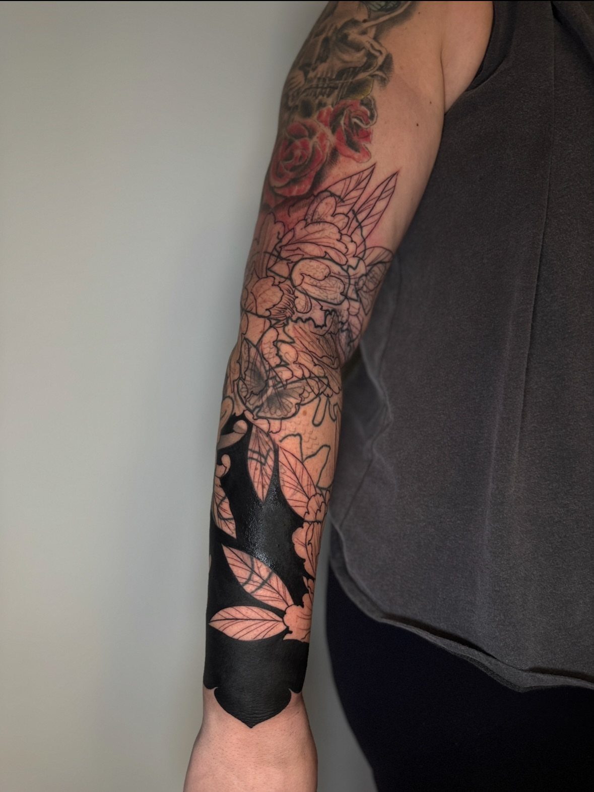 Tattooed arm showing a floral sleeve with a heavy black ink cover up section.