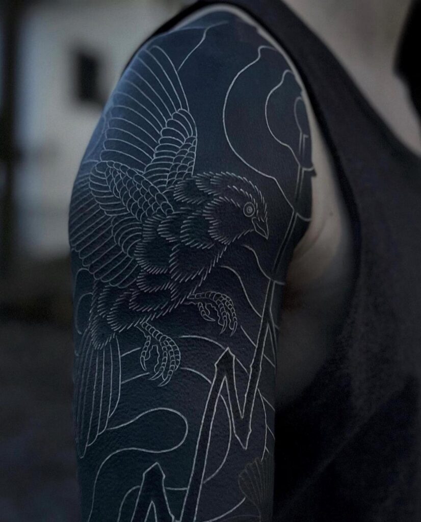 Detailed black ink tattoo of a bird on a person's muscular upper arm.