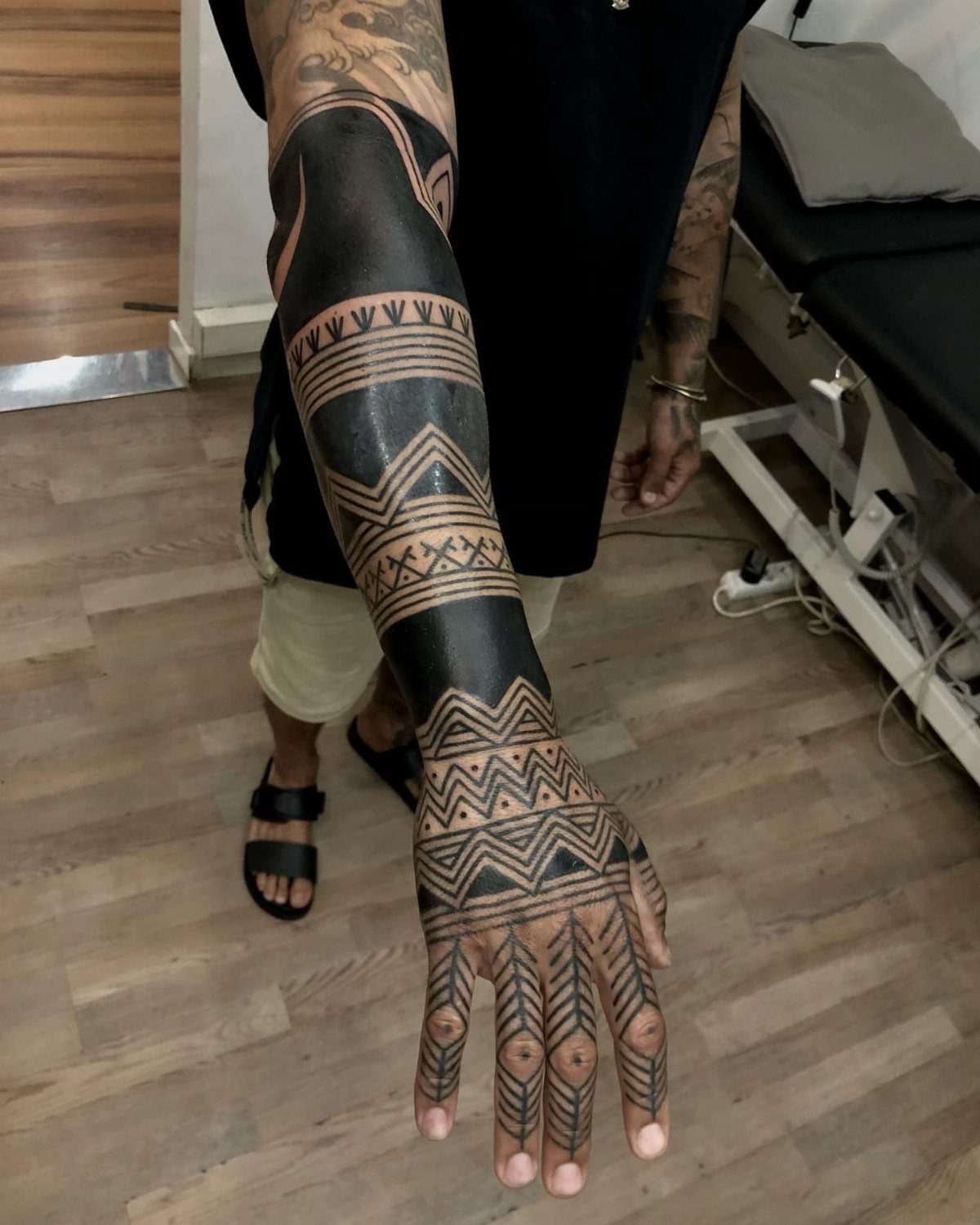 Tattooed arm and hand with bold black geometric tribal patterns and thick ink bands.
