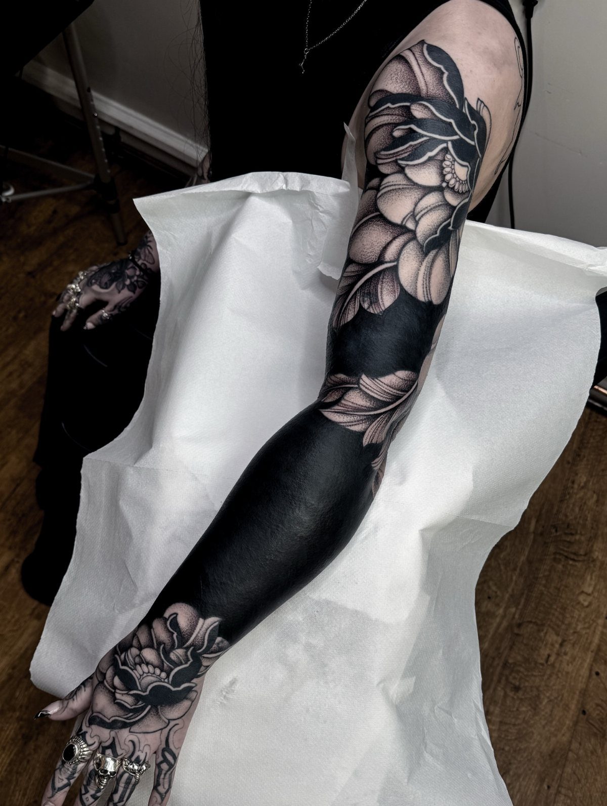 Blackout tattoo cover-up on an arm with grey floral designs on shoulder and hand