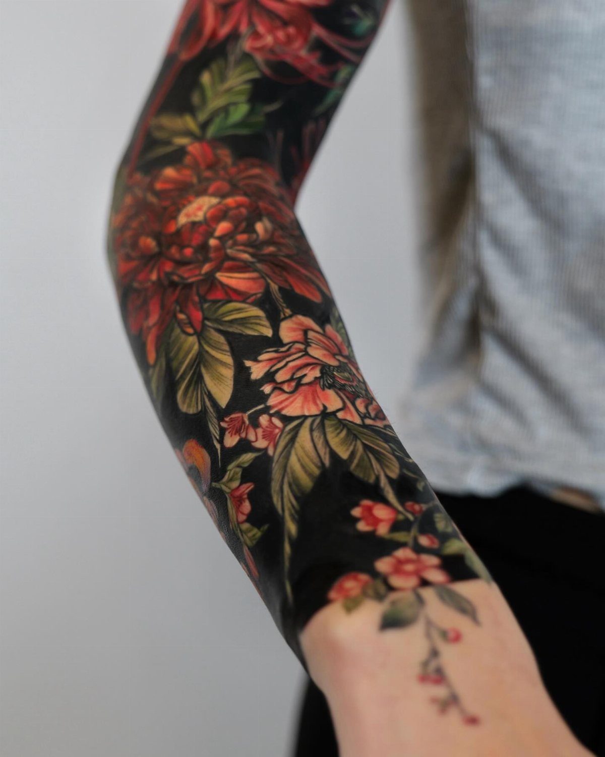 Arm sleeve tattoo with solid black background and red floral designs.