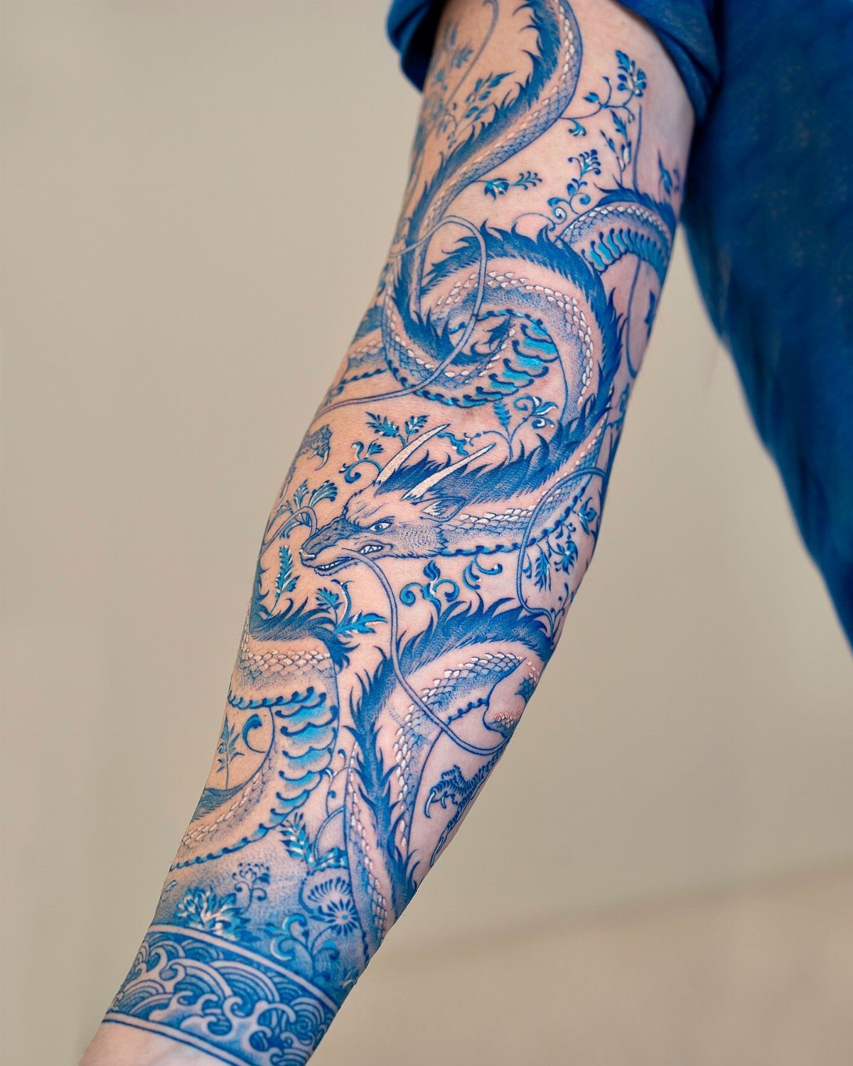 Blue ink dragon tattoo winding around a person's arm in traditional style.