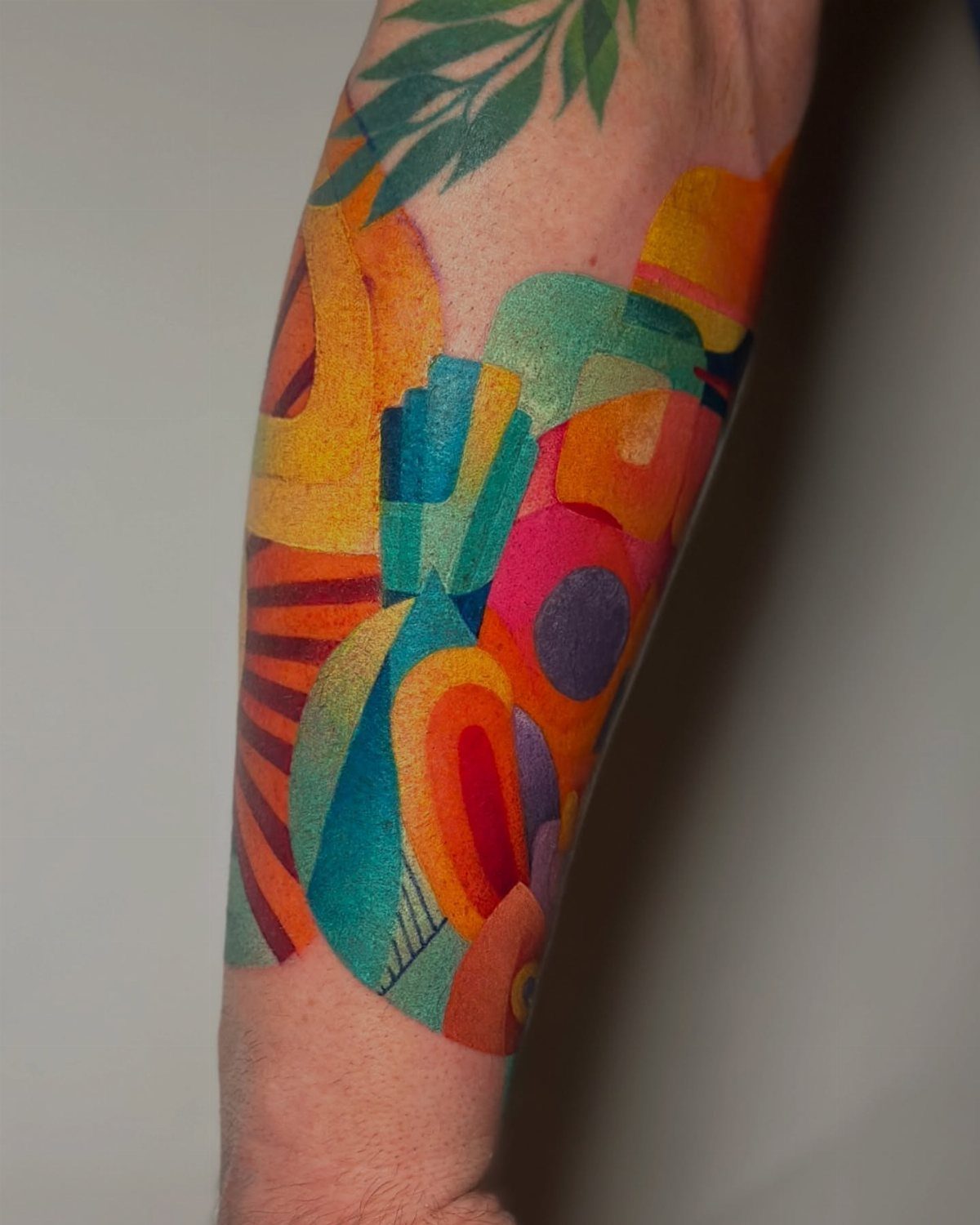 Abstract colorful tattoo on a forearm with vibrant geometric shapes and green leaves.