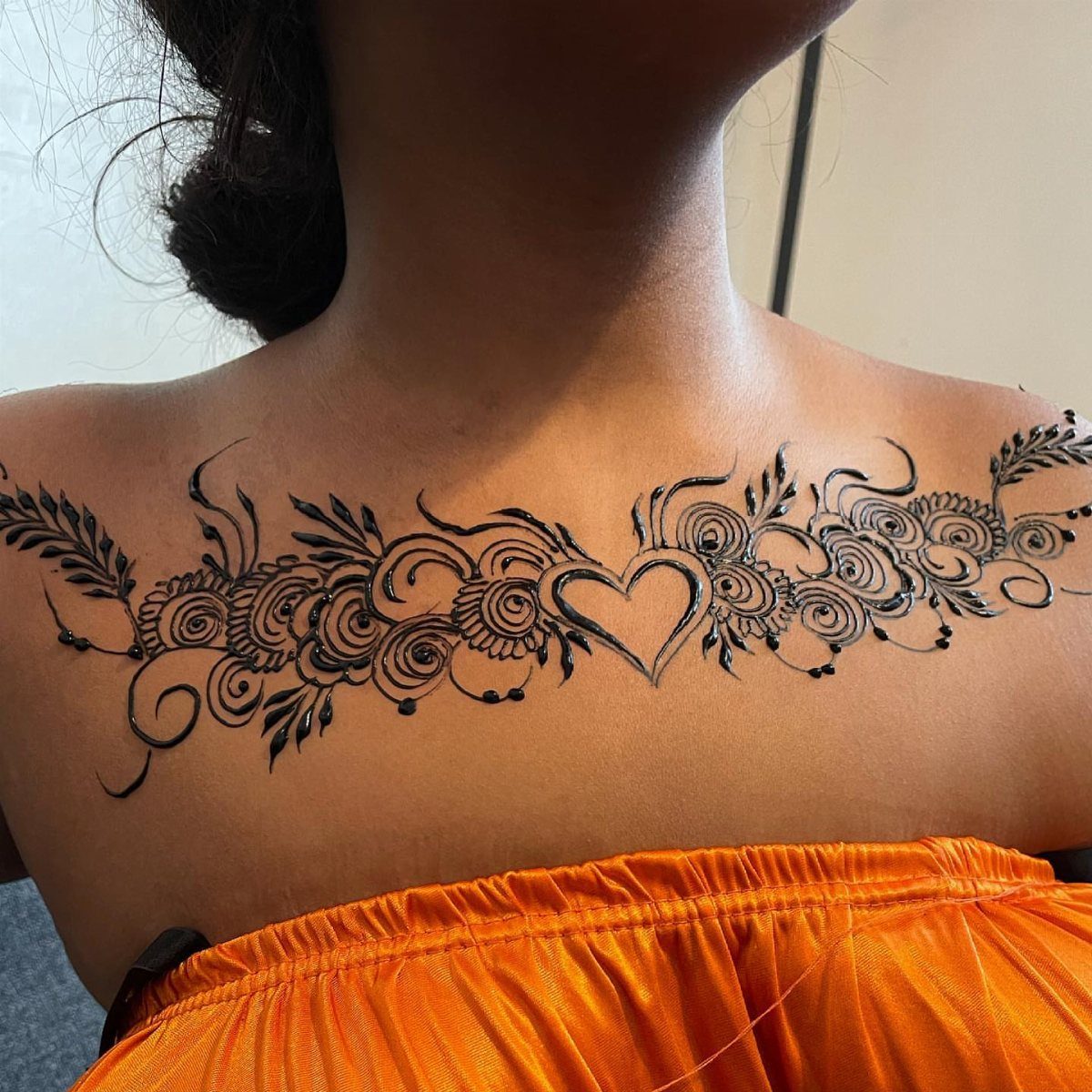 Intricate black henna tattoo with floral patterns and a heart on a chest.