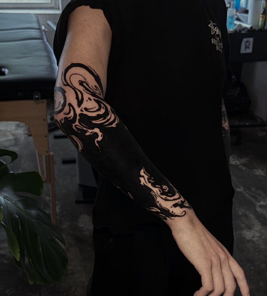 Solid black ink tattoo with swirling patterns covering a person's entire arm.