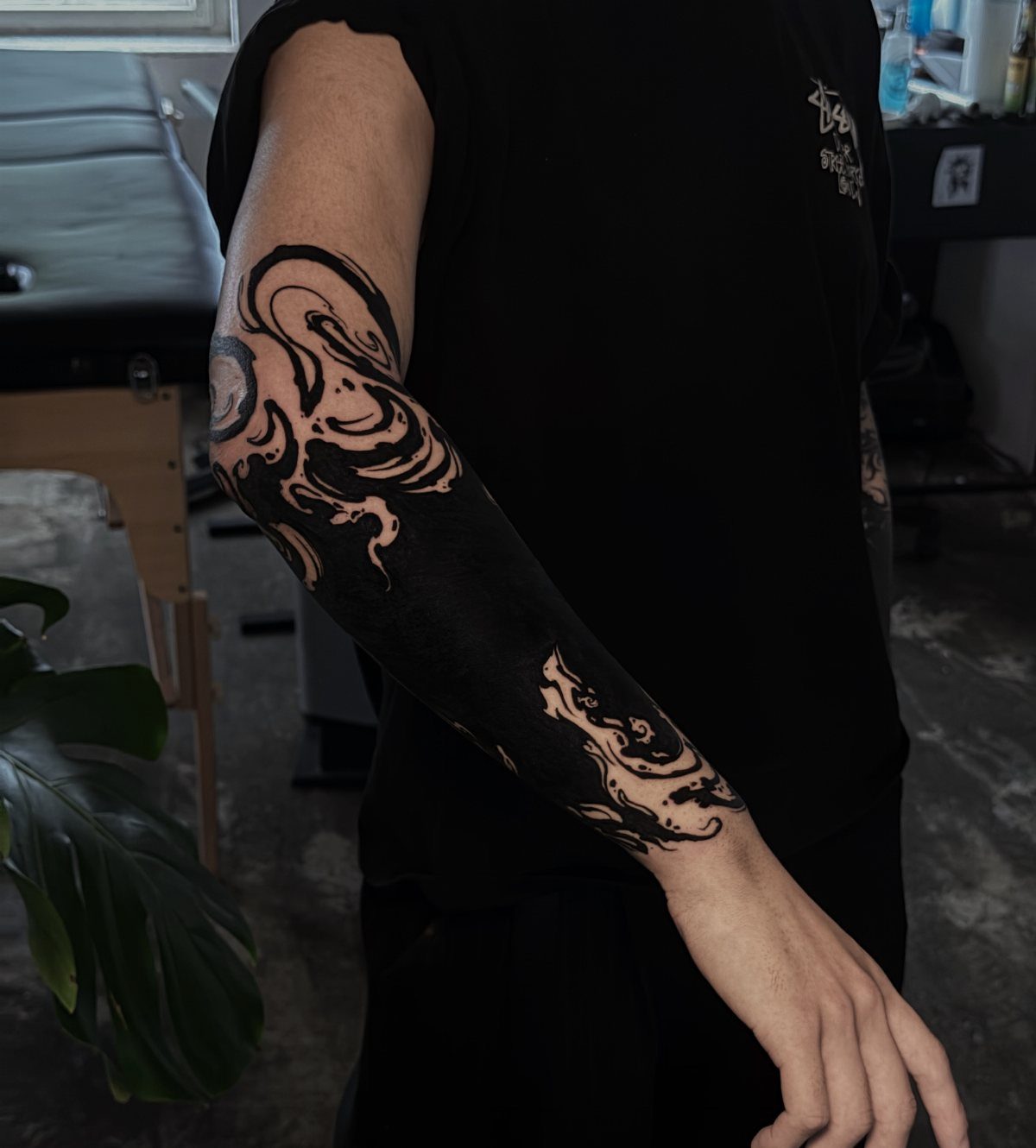 Solid black ink tattoo with swirling patterns covering a person's entire arm.