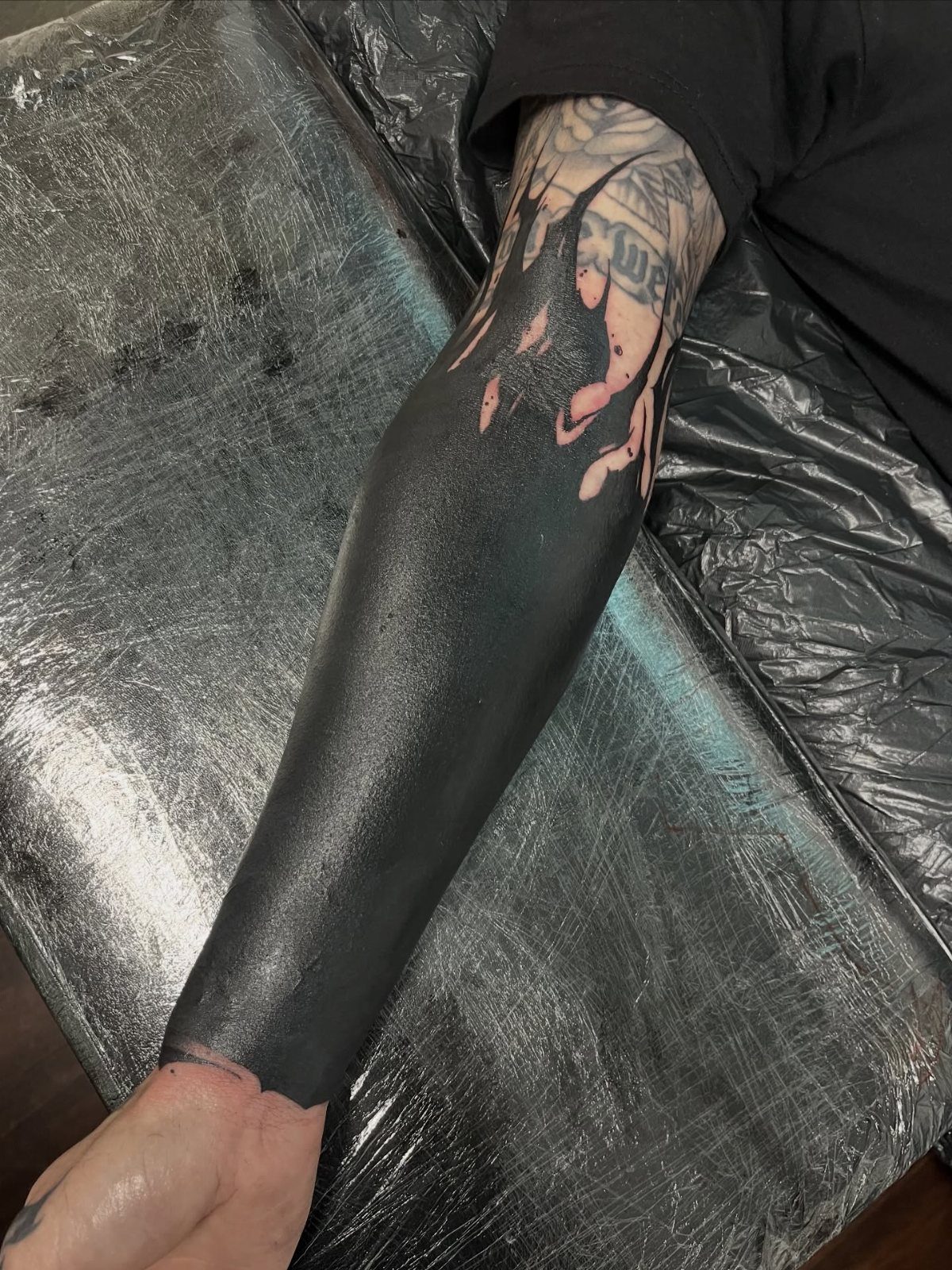 Forearm with a solid black ink blackout tattoo covering previous ink designs.