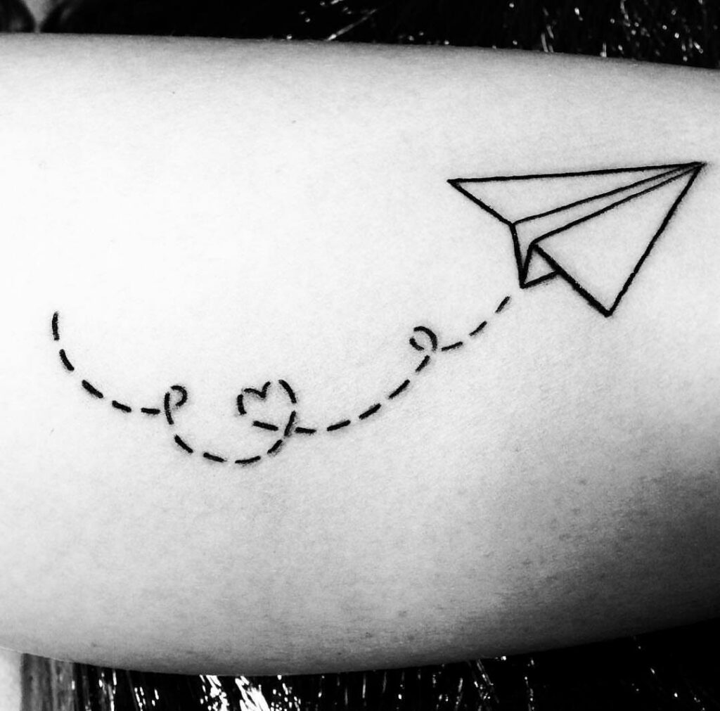 Paper airplane tattoo with a dashed line and small heart on skin