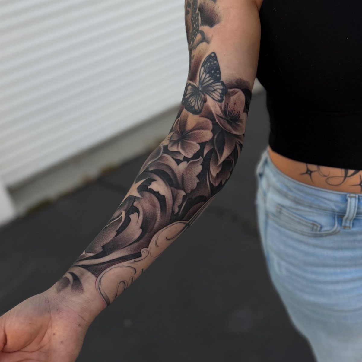 Black and grey floral tattoo with a butterfly covering a person's entire forearm.