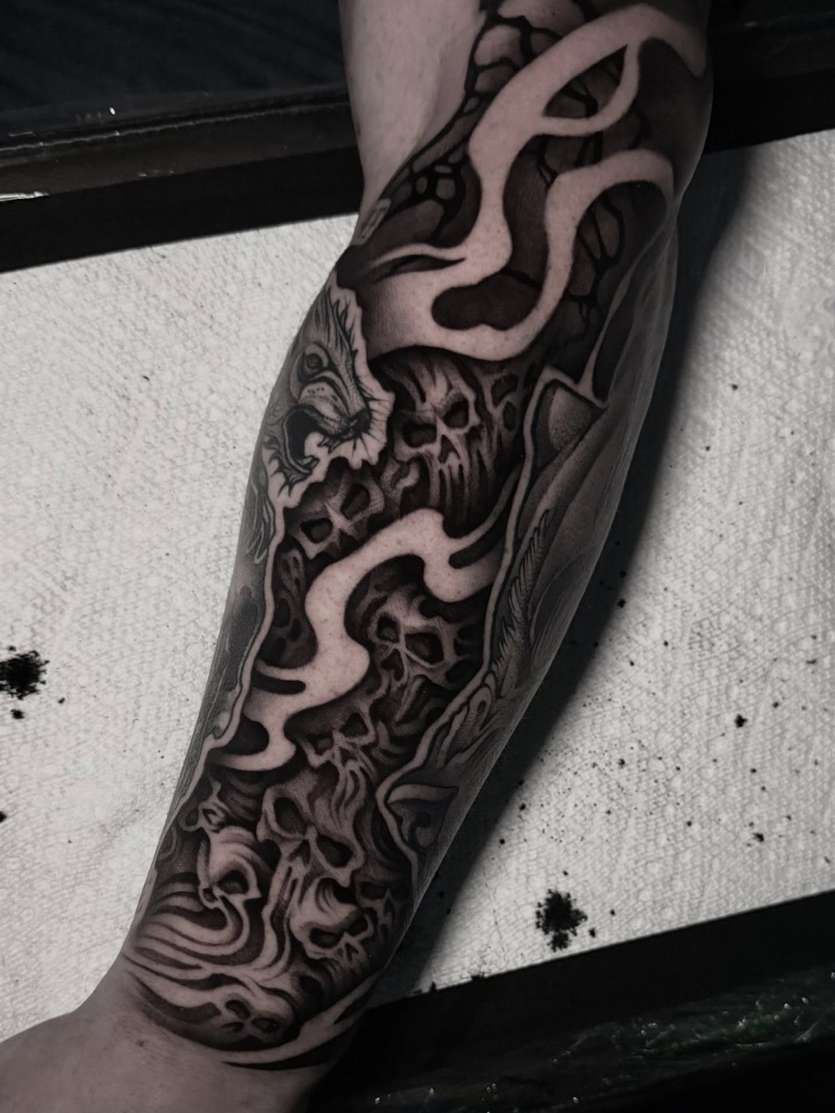 Forearm tattoo featuring black and grey skulls with flowing organic filler patterns.