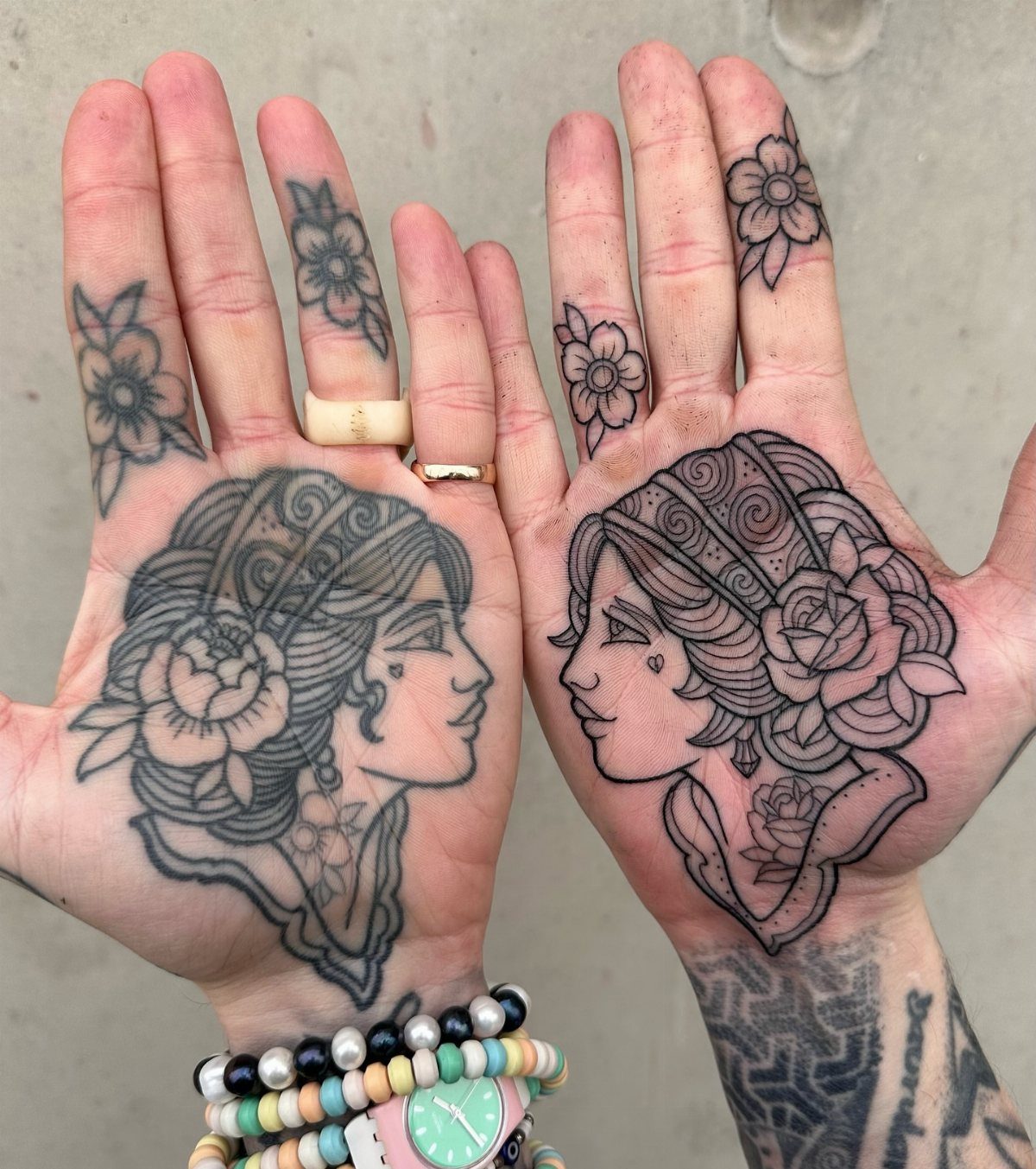 Two open palms with large portrait tattoos and smaller floral finger tattoos.