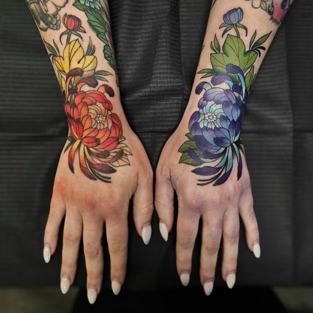 Neo-traditional floral tattoos on two hands featuring red and purple blossoms with leaves.