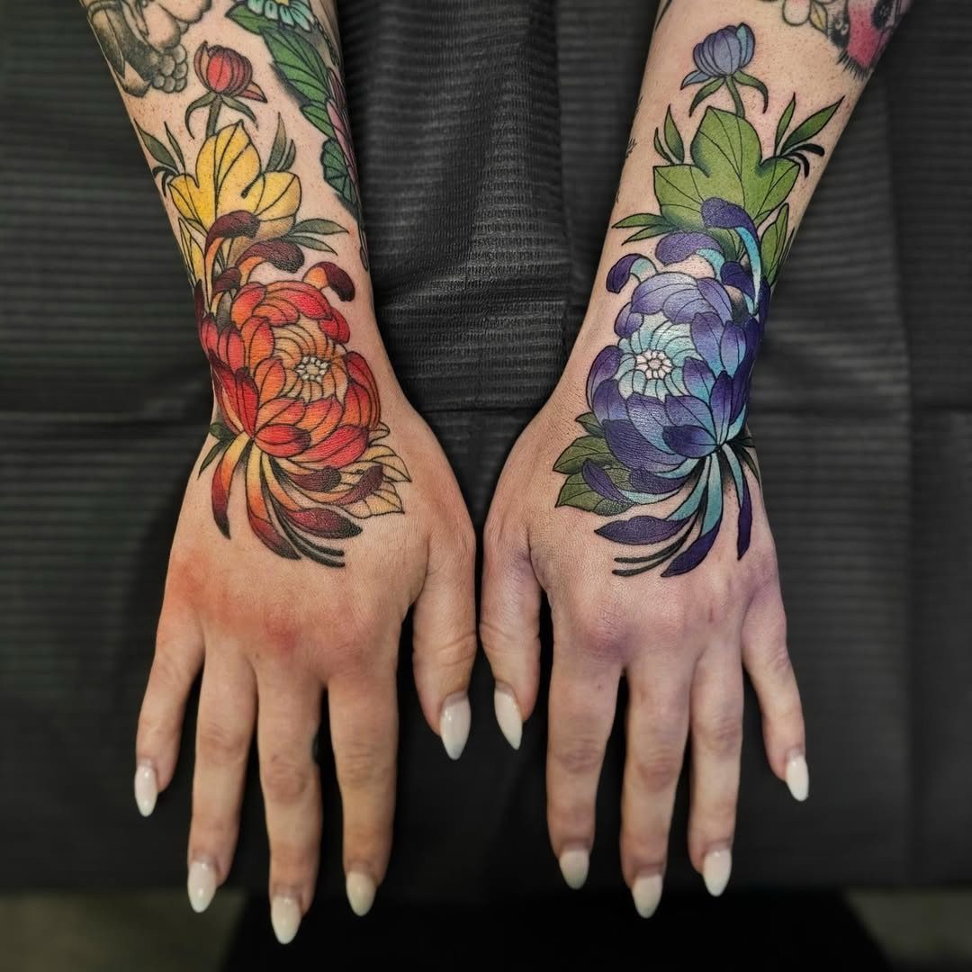 Neo-traditional floral tattoos on two hands featuring red and purple blossoms with leaves.