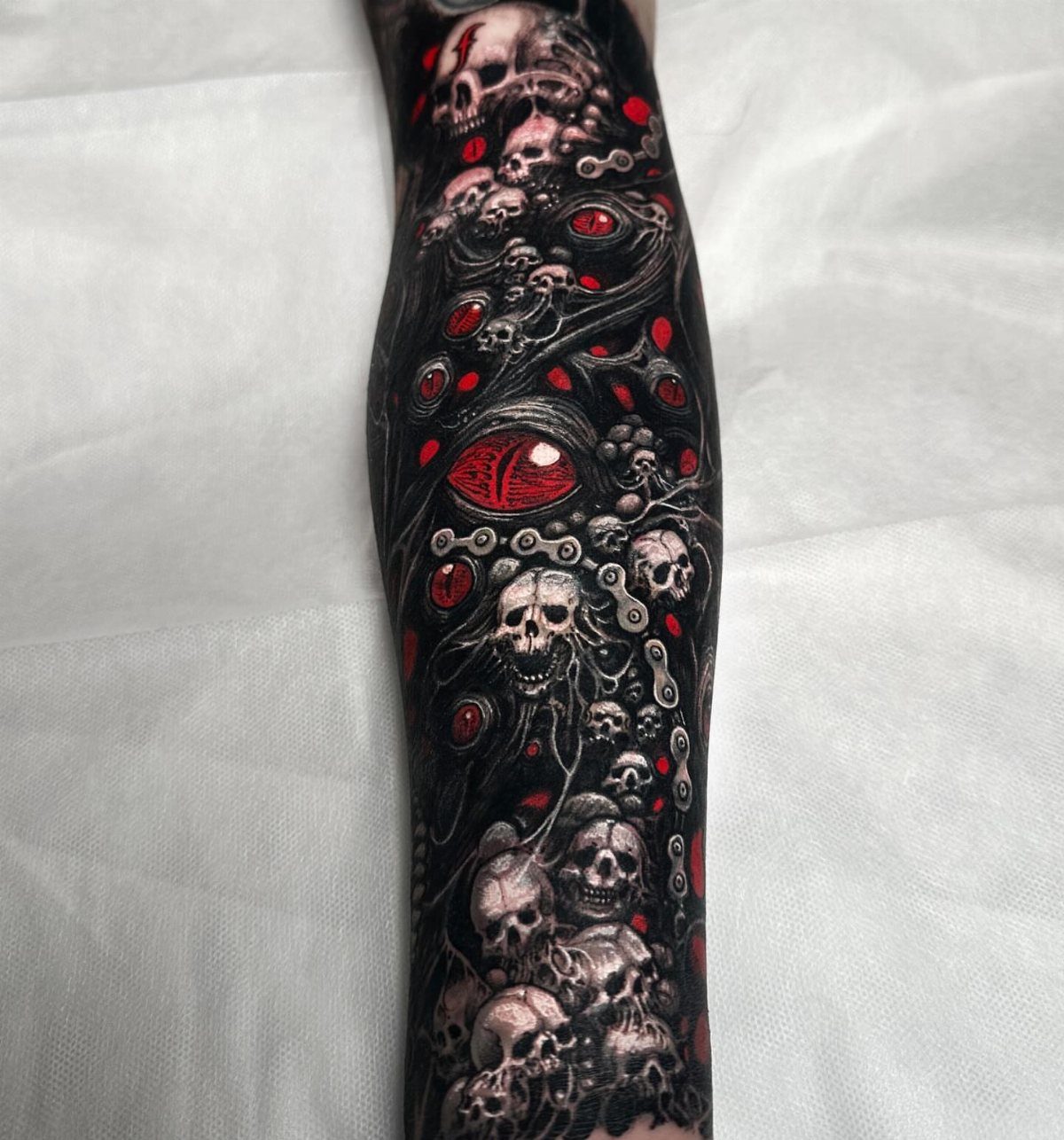 Full sleeve tattoo featuring multiple detailed skulls and red eyes in dark ink.