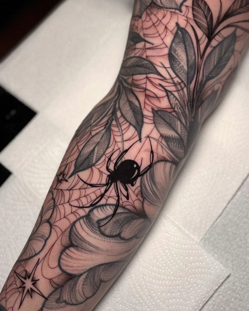 Tattooed arm showing a spider and webs filling gaps between leaf designs.