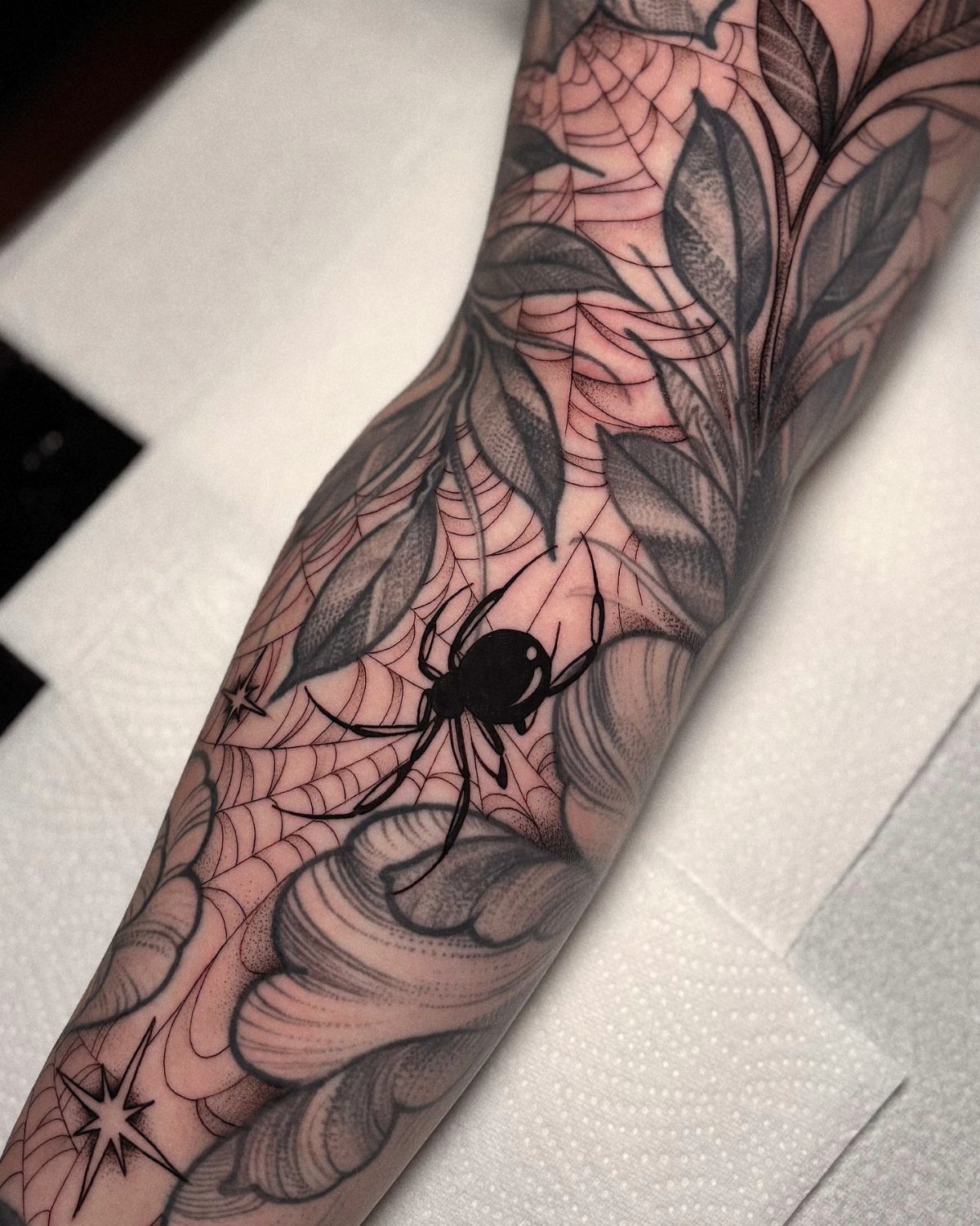 Tattooed arm showing a spider and webs filling gaps between leaf designs.