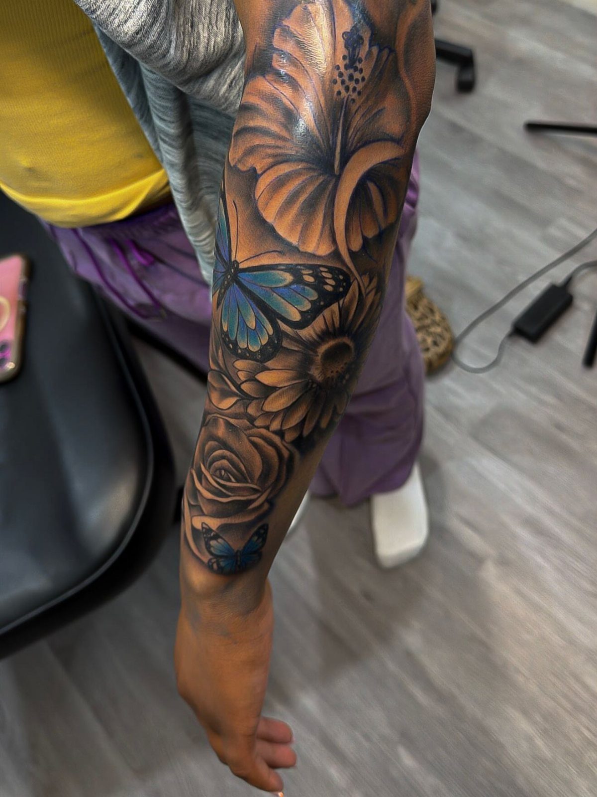Tattoo sleeve on a forearm featuring a blue butterfly and floral filler designs.