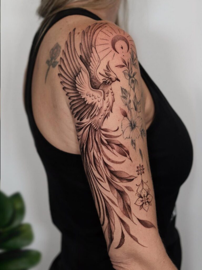Phoenix tattoo with a crescent moon and flowers on a person's upper arm.