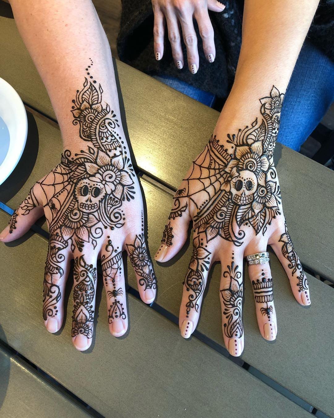 Henna skull tattoos with intricate floral patterns on the backs of two hands.