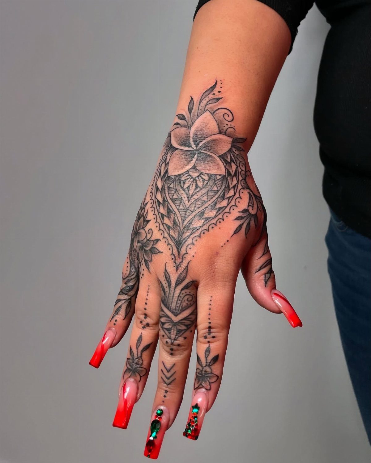 Hand with intricate black henna style tattoos and long red acrylic nails.