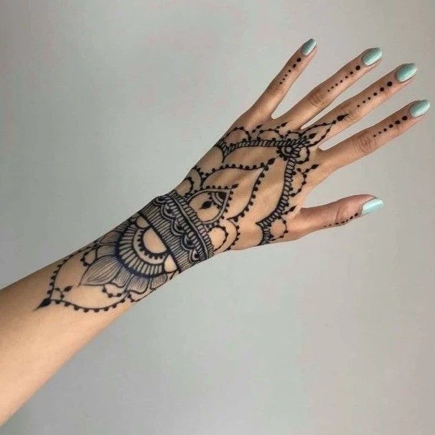 Intricate henna tattoo on a hand and wrist with light blue nail polish.