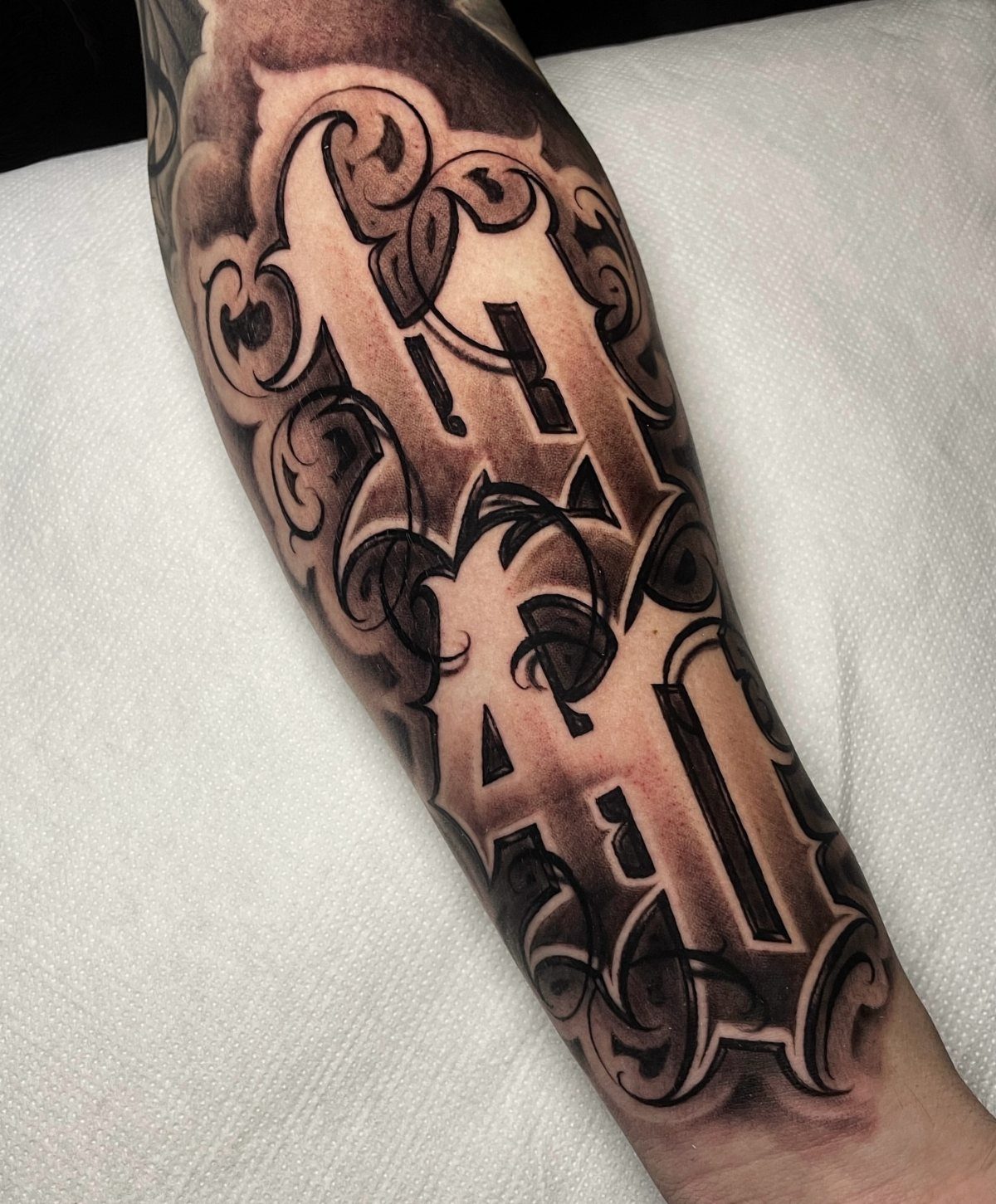 Stylized black and grey letter tattoo with negative shading on a person's forearm