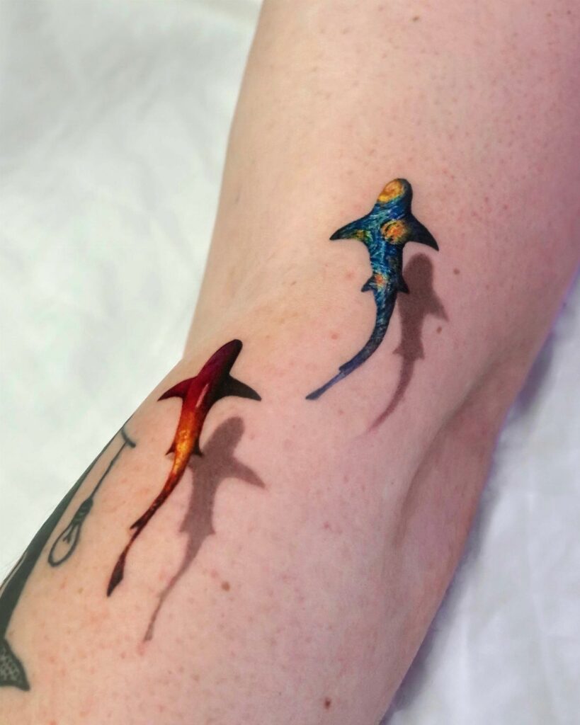 Two colorful 3D shark tattoos with shadows on a person's arm.