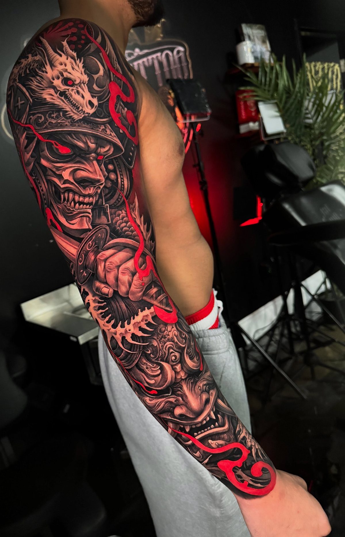 Full sleeve tattoo of a samurai skull and dragon in red and black ink.