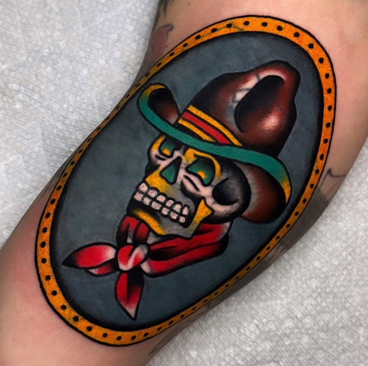 Skull tattoo with a brown hat and red bandana in traditional style.
