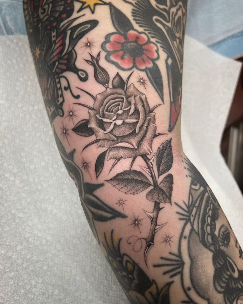 Detailed black and grey rose tattoo on a person's arm among other tattoos.