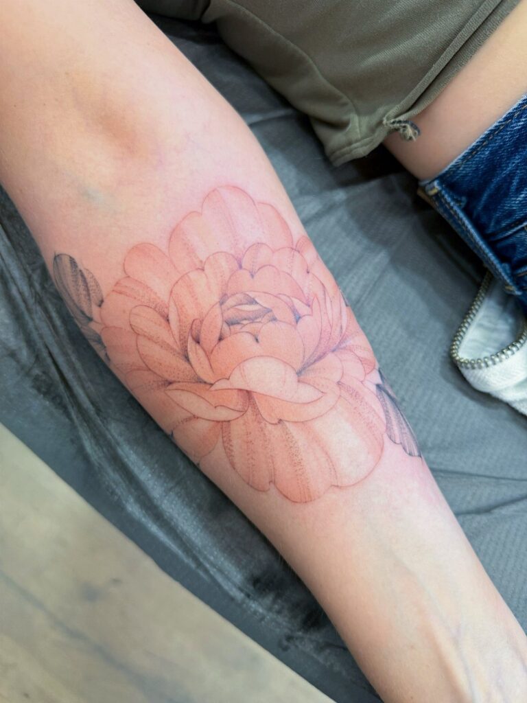 Peach-colored flower tattoo with soft shading on a person's forearm.