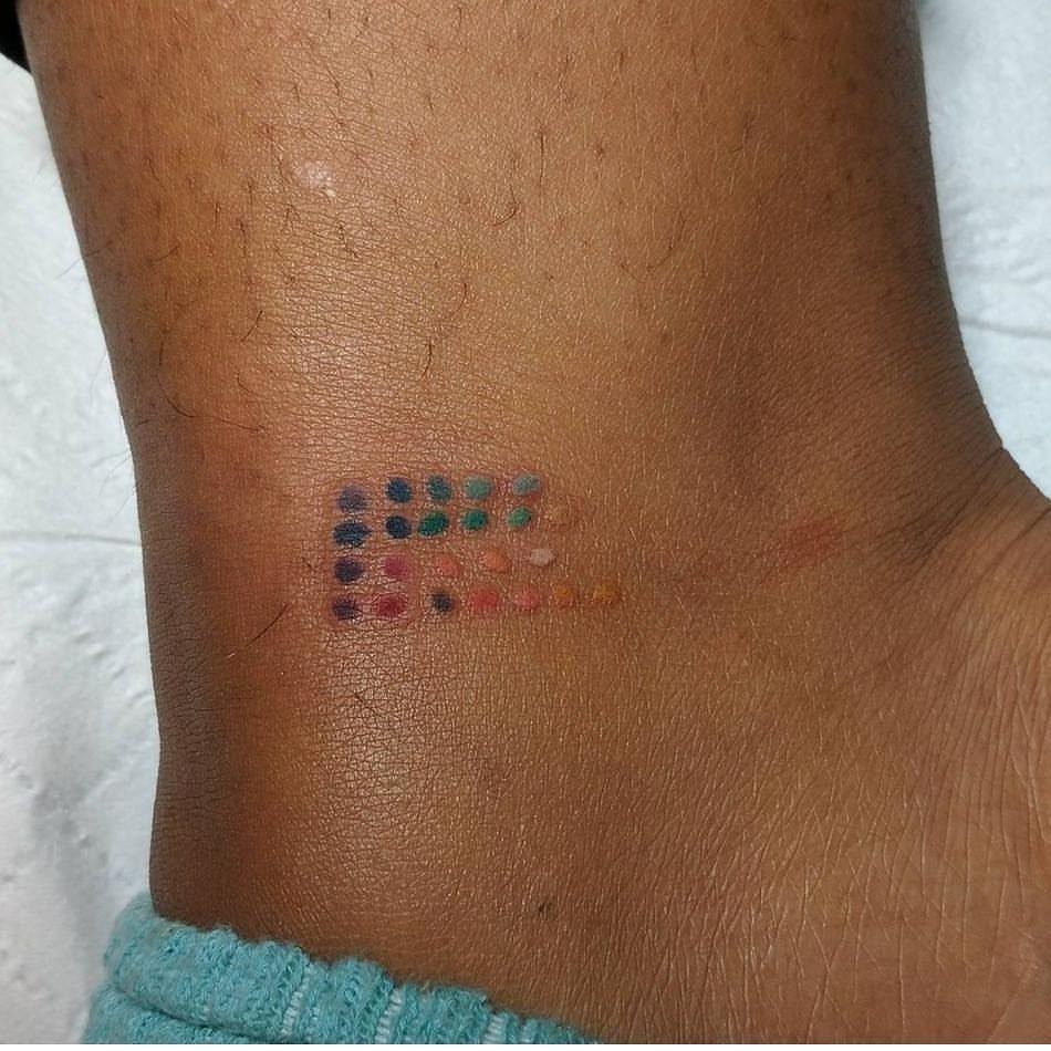 Grid of colorful tattoo ink test dots on brown skin of an ankle