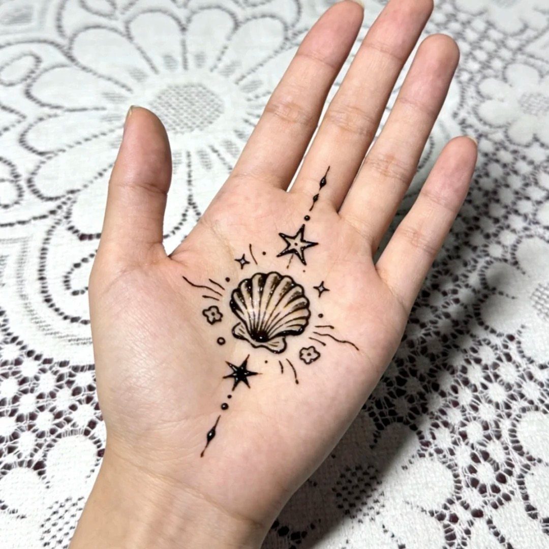 Small henna tattoo of a seashell and stars on a person's open palm.