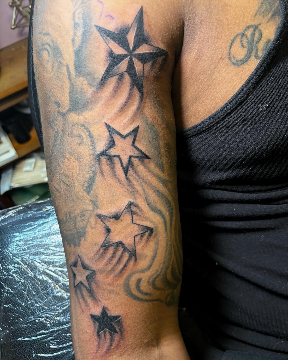 Black ink star tattoos of various sizes on a person's upper arm.