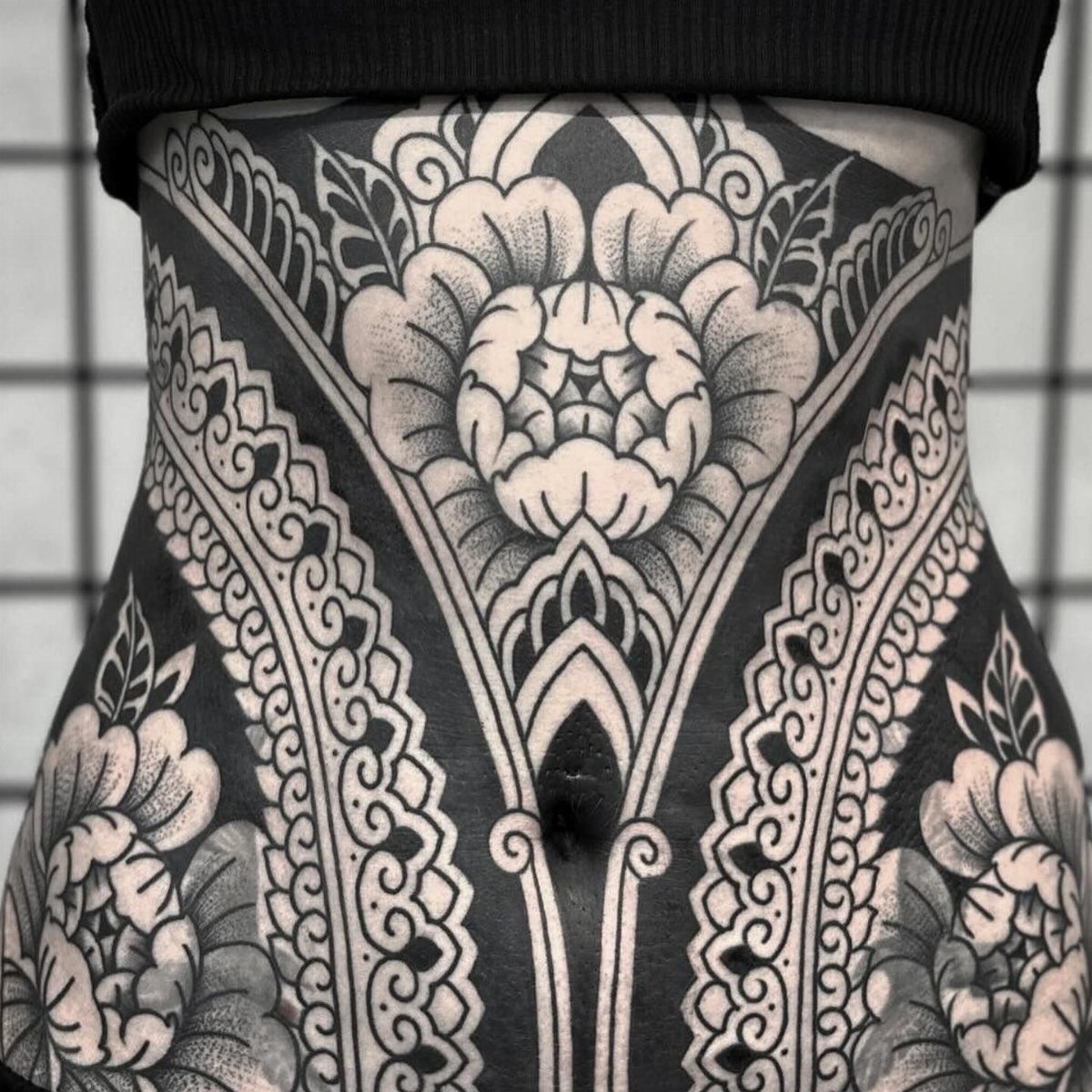 Symmetrical black and grey floral tattoo covering a person's stomach area
