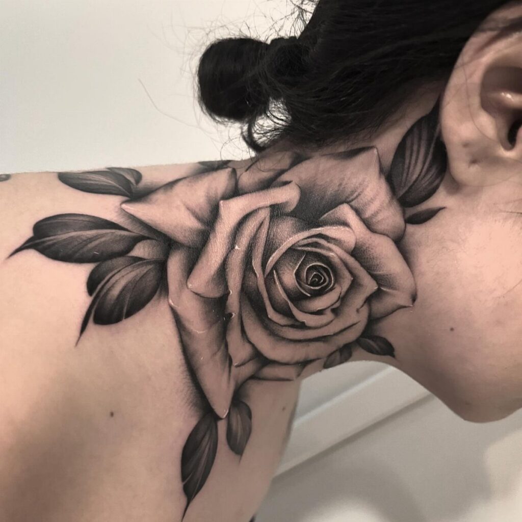 Large black and grey rose tattoo on a person's neck and shoulder.