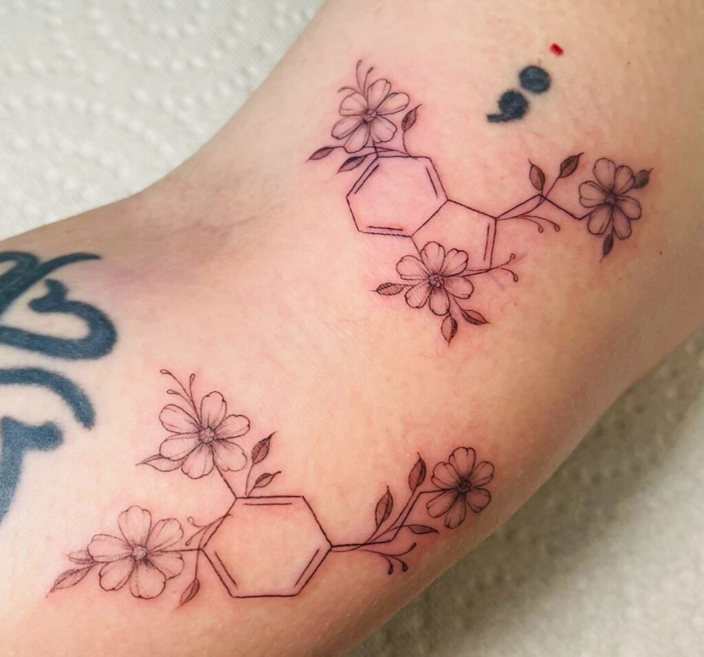 Serotonin chemical structure tattoo integrated with delicate flowers on a person's skin
