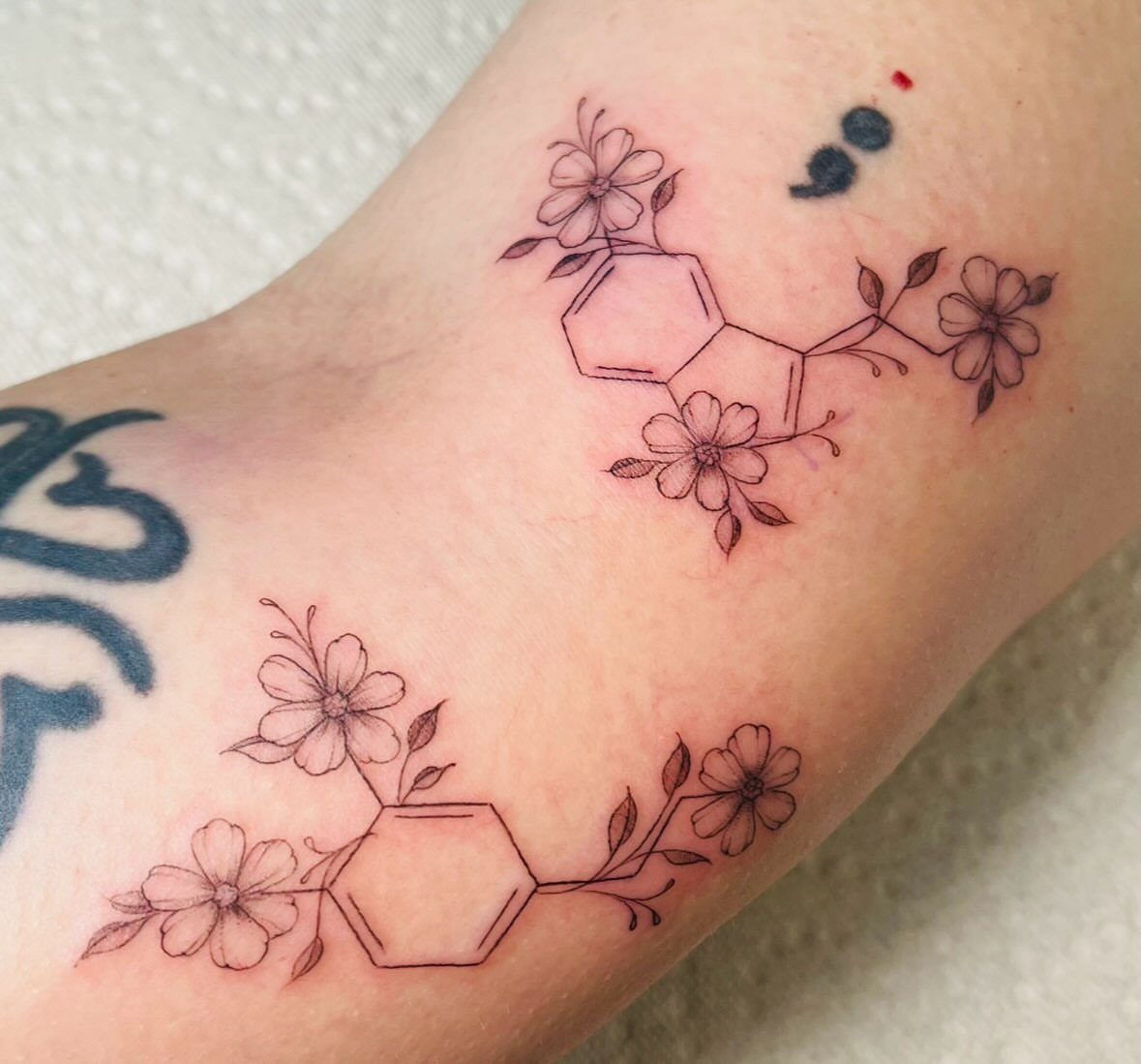 Serotonin chemical structure tattoo integrated with delicate flowers on a person's skin