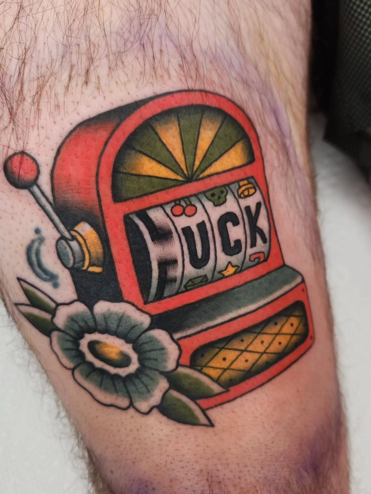 Red slot machine tattoo with the word LUCK and a white flower on skin.