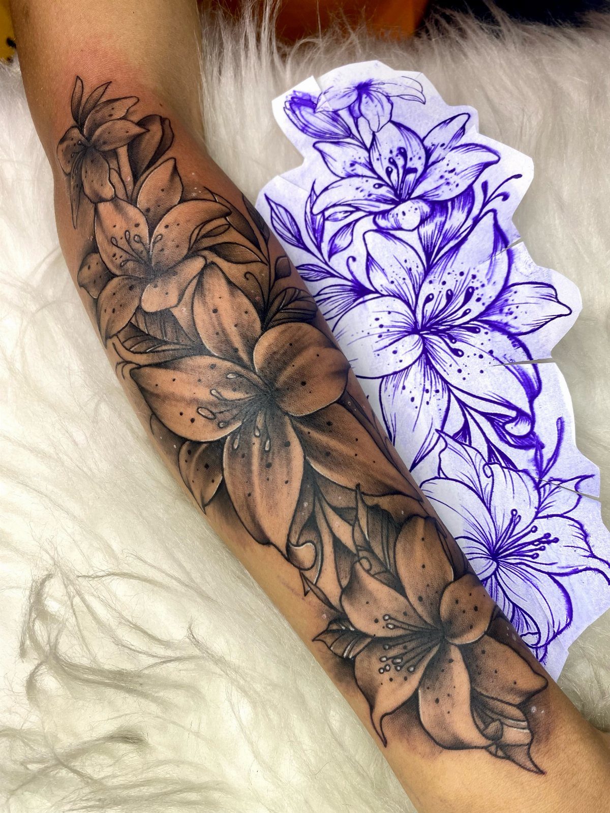 Lily flower tattoo on a forearm next to its purple ink stencil.