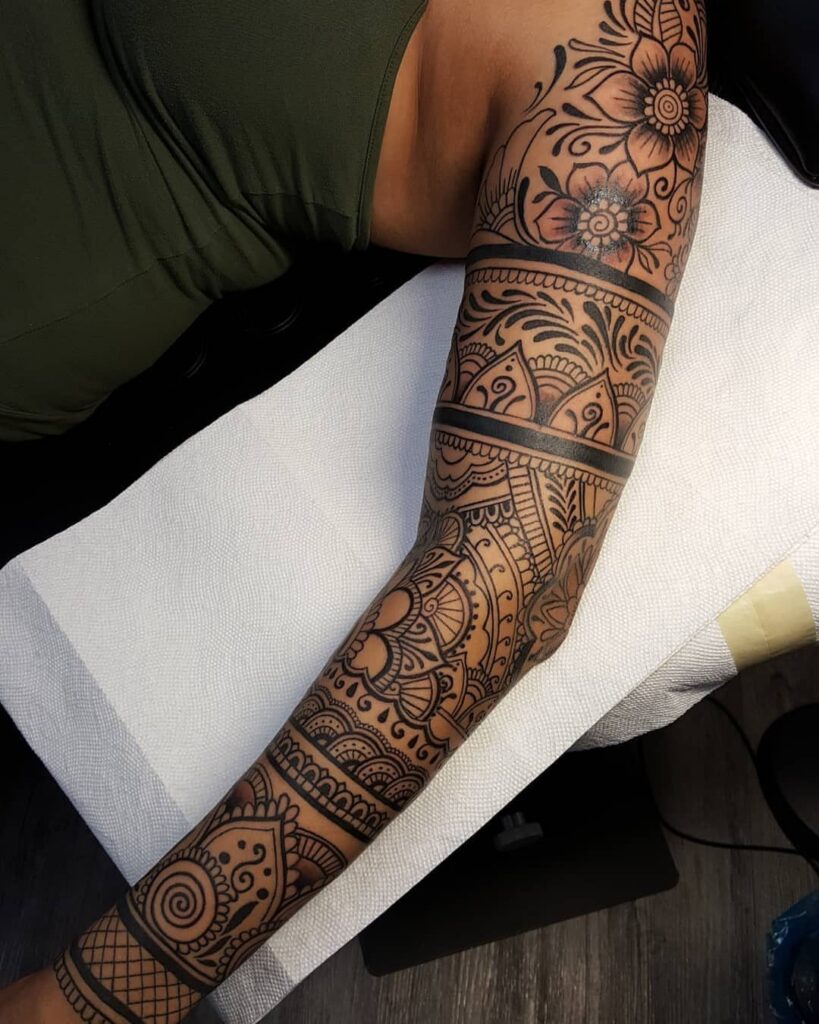 Intricate henna-style tattoo with floral and mandala patterns covering a person's arm and shoulder.