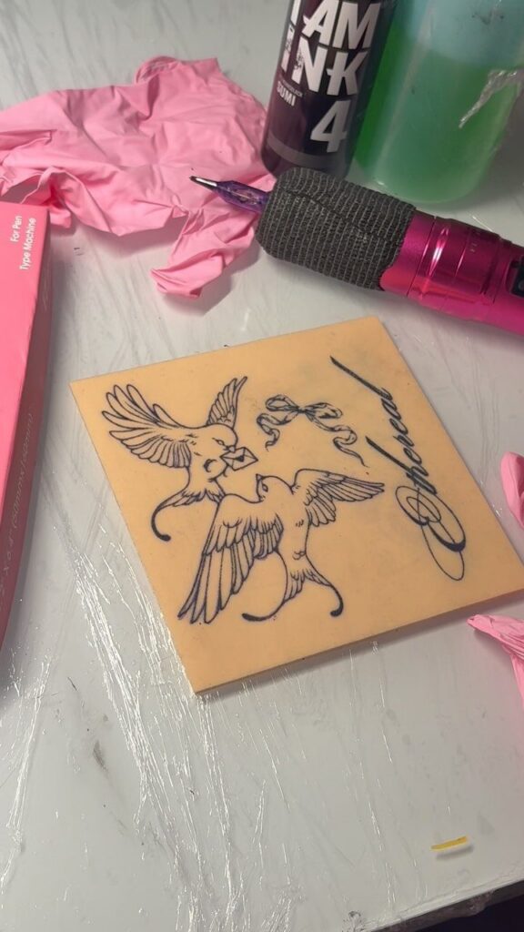 Tattoo of two birds on a square of tan fake skin with equipment.