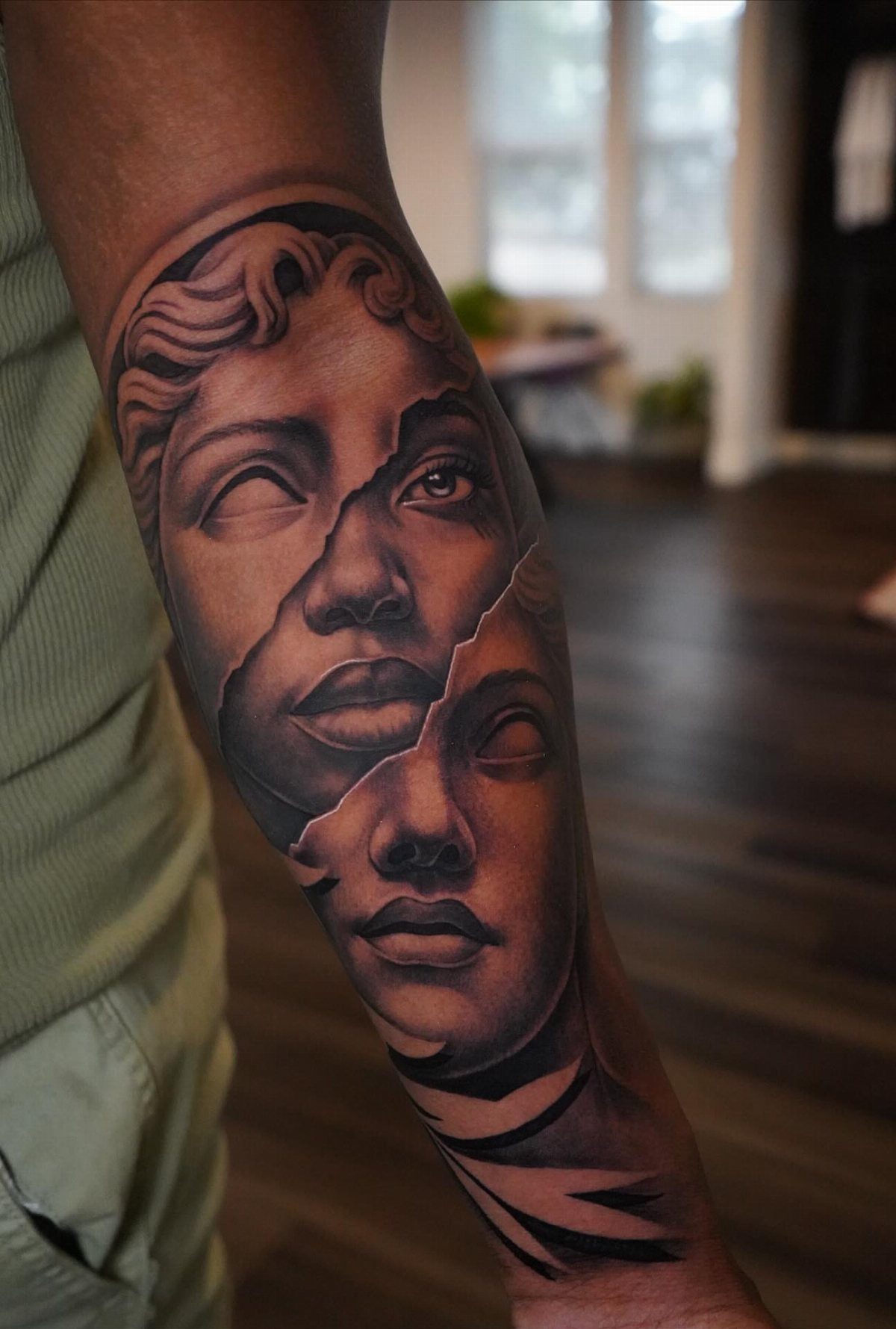 Detailed black and grey tattoo of a cracked sculpture face on dark skin.
