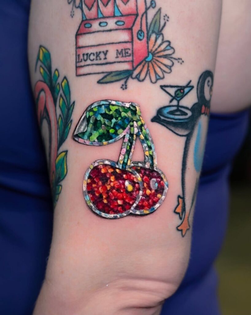 Cherry tattoo with a white border and glittery finish on a person's arm.