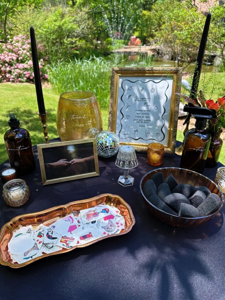 Temporary tattoo station with tattoo sheets, sponges, and apothecary bottles on a black table.