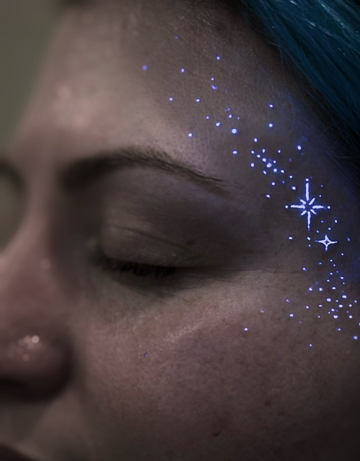 Glowing blue UV ink star tattoos on a person's cheek and temple