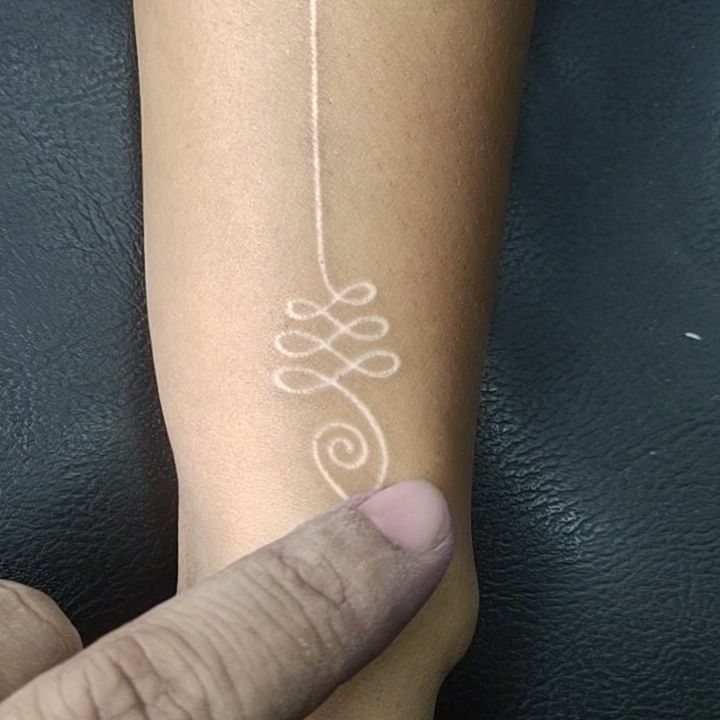 White ink tattoo of a spiral swirl on a person's forearm skin.