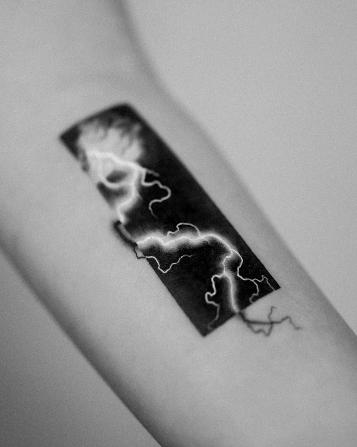 Jagged white lightning bolt tattoo striking through a solid black rectangular block on skin.